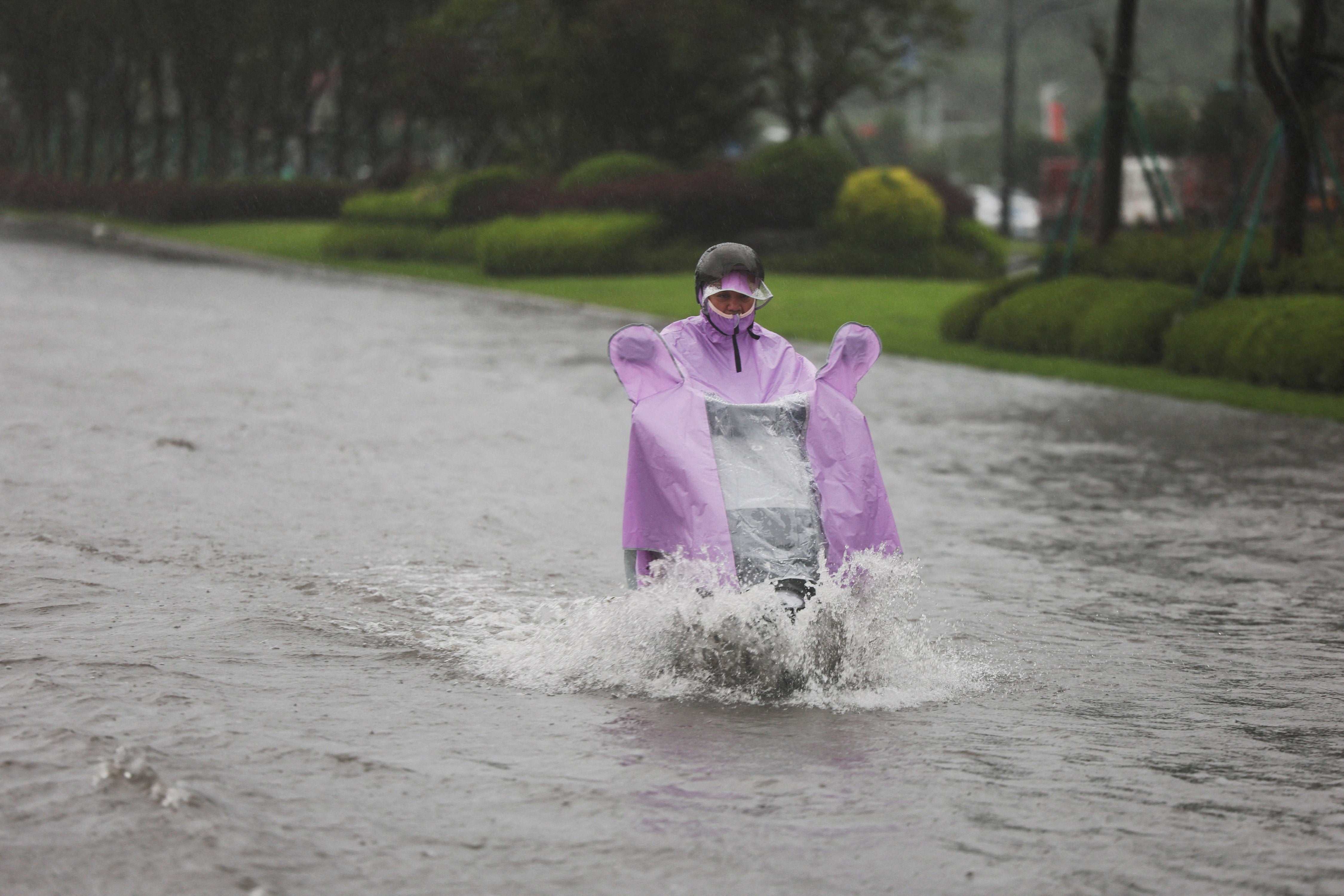 A person rides an electric scooter through a flooded road after heavy rain brought by Typhoon Bavi in Wenzhou, Zhejiang province, China