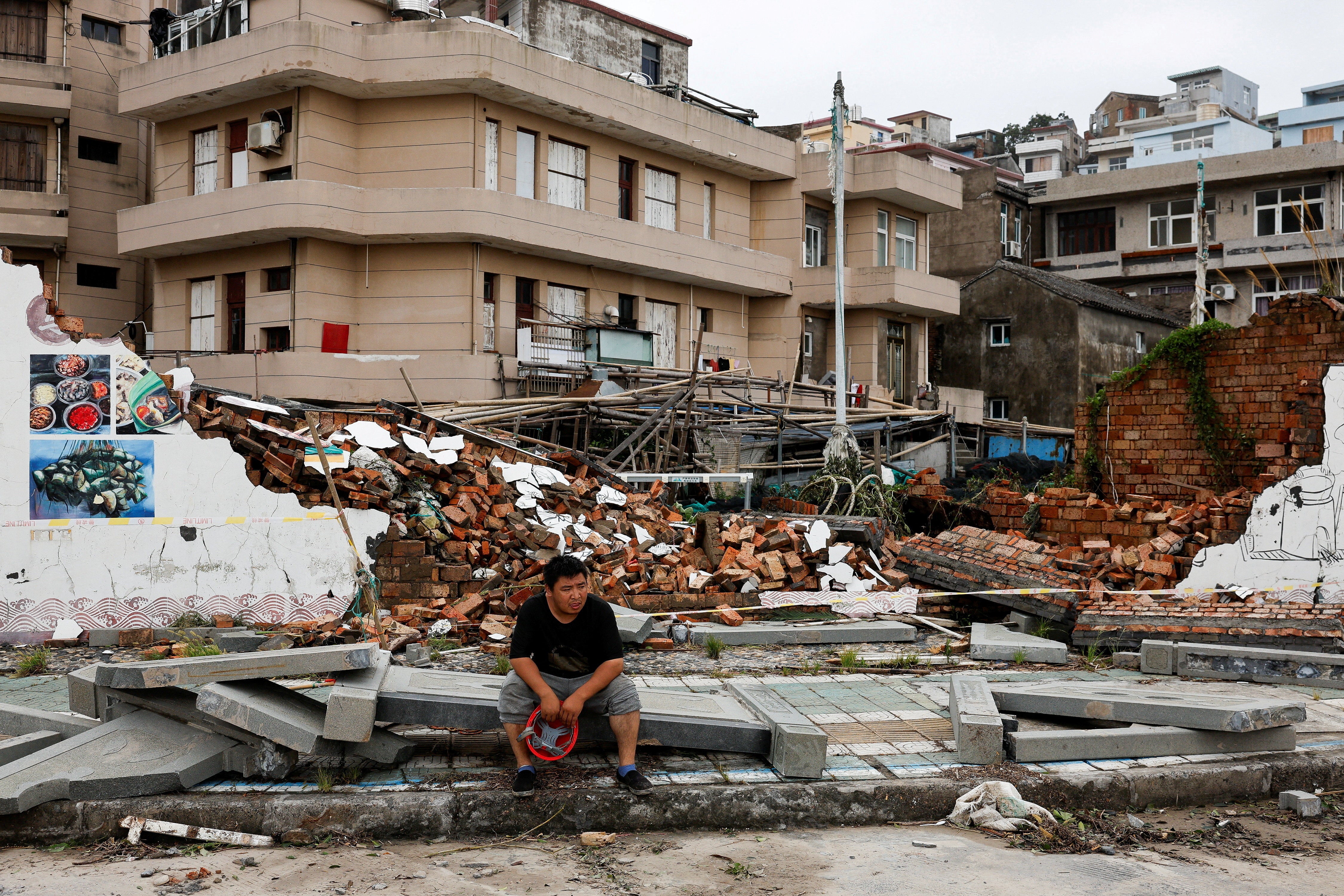 A person sits beside a collapsed wall in the aftermath of Typhoon Bavi in the coastal village of Dongsha, Taizhou, Zhejiang province, China