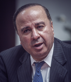 A photograph of a man with dark hair in a suit as he's talking.