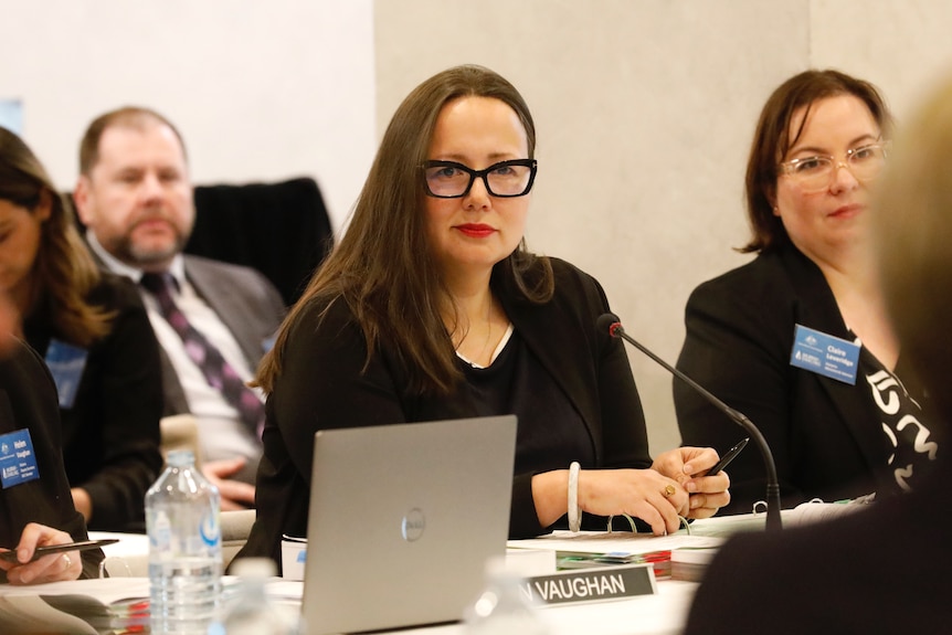 A woman with bold glasses sits at a table.