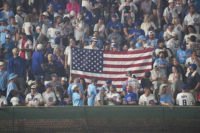 Fans hold a United States flag in the bleachers during the sixth inning of a baseball game between the Chicago Cubs and the St. Louis Cardinals, Saturday, July 4, 2026, in Chicago. (AP Photo/David Banks)