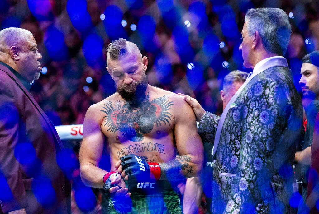 Conor McGregor is consoled by Bruce Buffer in the octagon receiving an injured leg after a quic ...