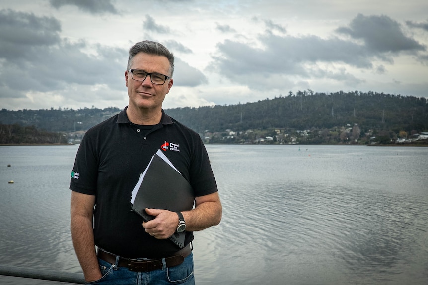 A man holds a clipboard while standing near a waterway.