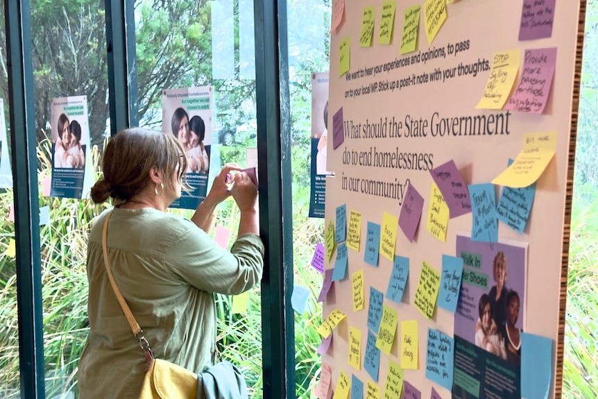 A woman writes on a sticky note at the Walk in Her Shoes next to a placard reading