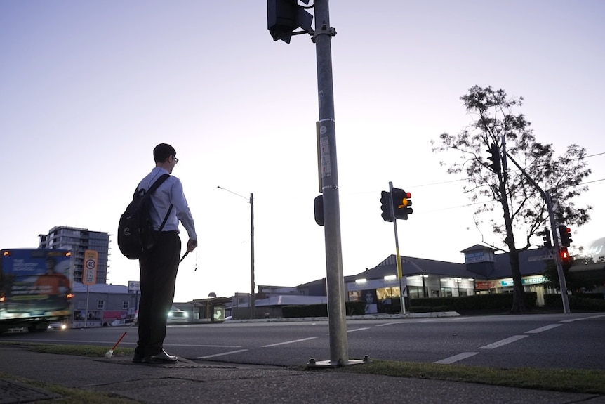 Sam stands at a traffic intersection waiting, holding his cane.