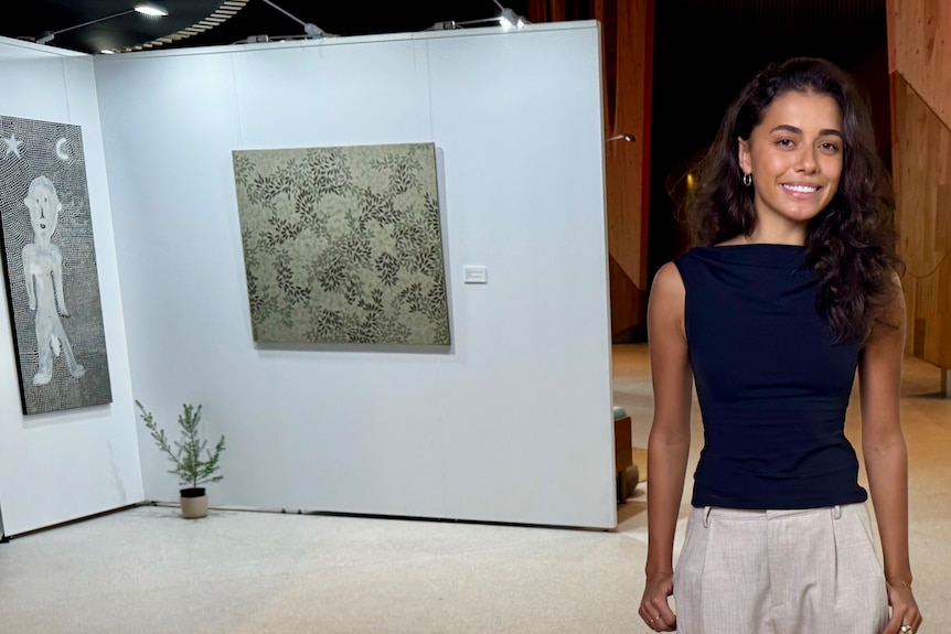 A woman stands next to artworks.
