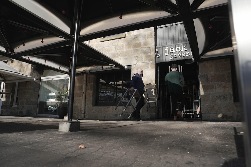 Two male staffmembers bringing chairs inside from an empty venue.