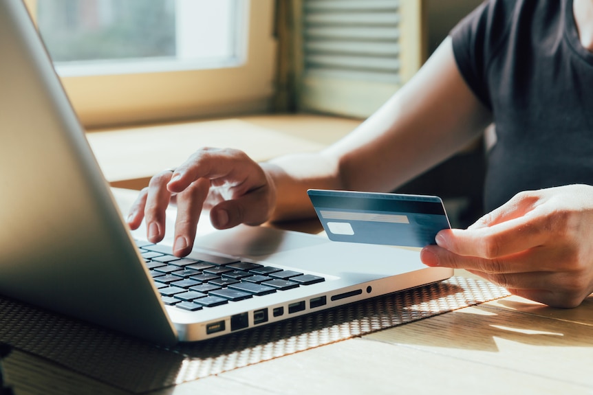 A woman's arms are pictured - one typing on a laptop while the other holds a credit card.