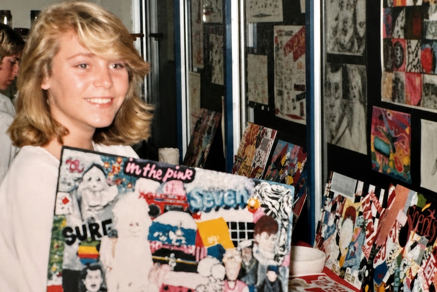 Young girl smiles with scrapbooked art in front of wall of exhibit