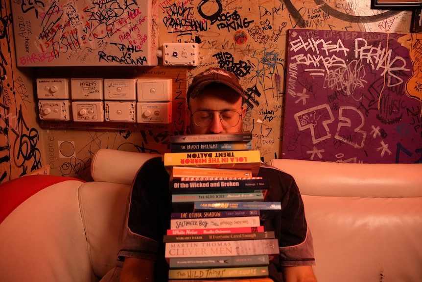 A man sitting down leaning his head on a pile of books, eyes closed, reading glasses
