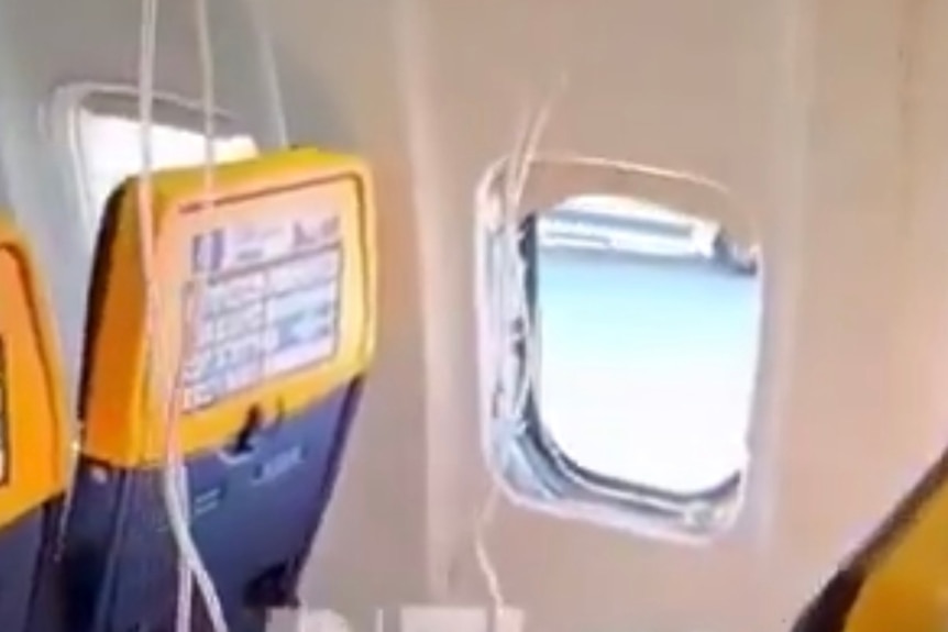 A blurry photo shows an airplane window with air masks hanging from the ceiling.