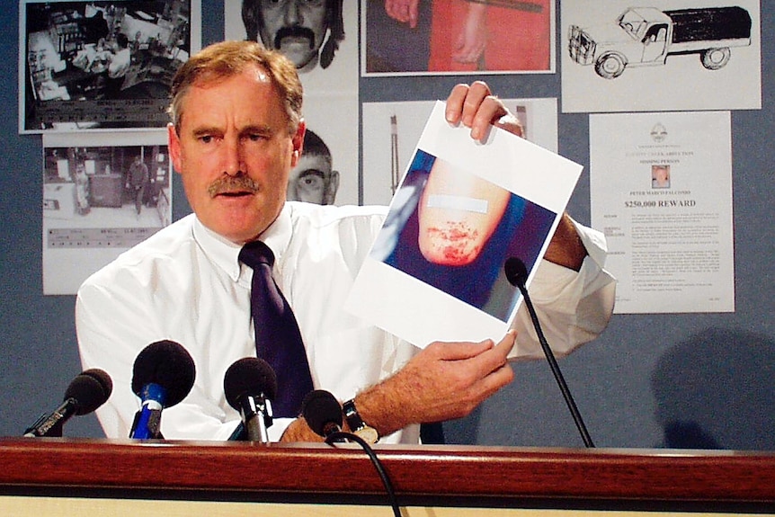 A police officer holding up a photo of a bloodied elbow.