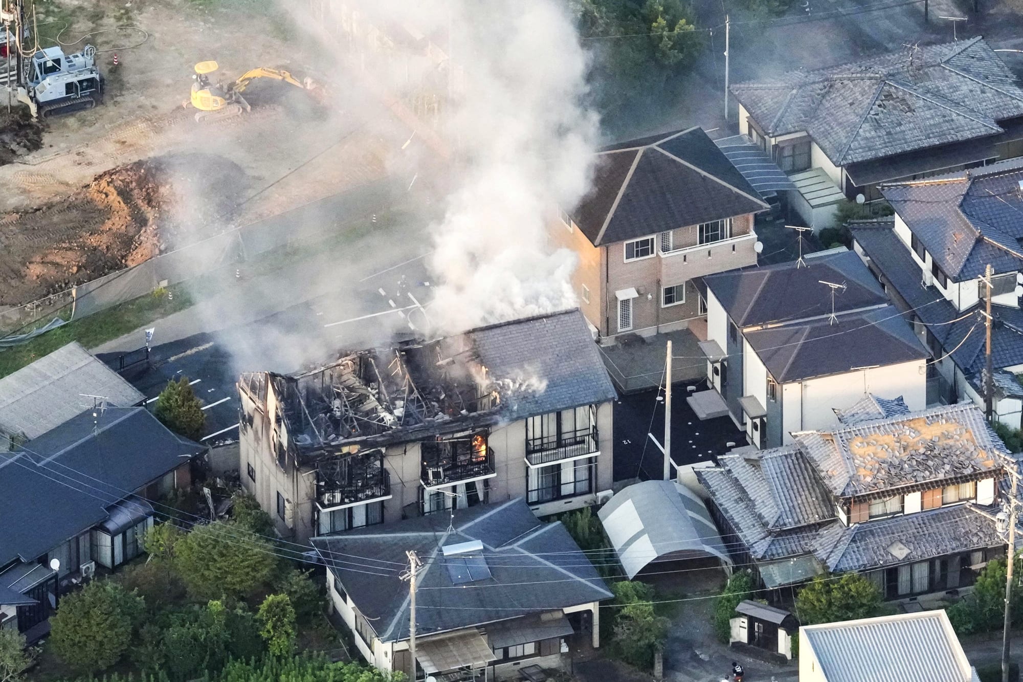 An aerial view of a damaged house with smoke rising out of the exposed roof