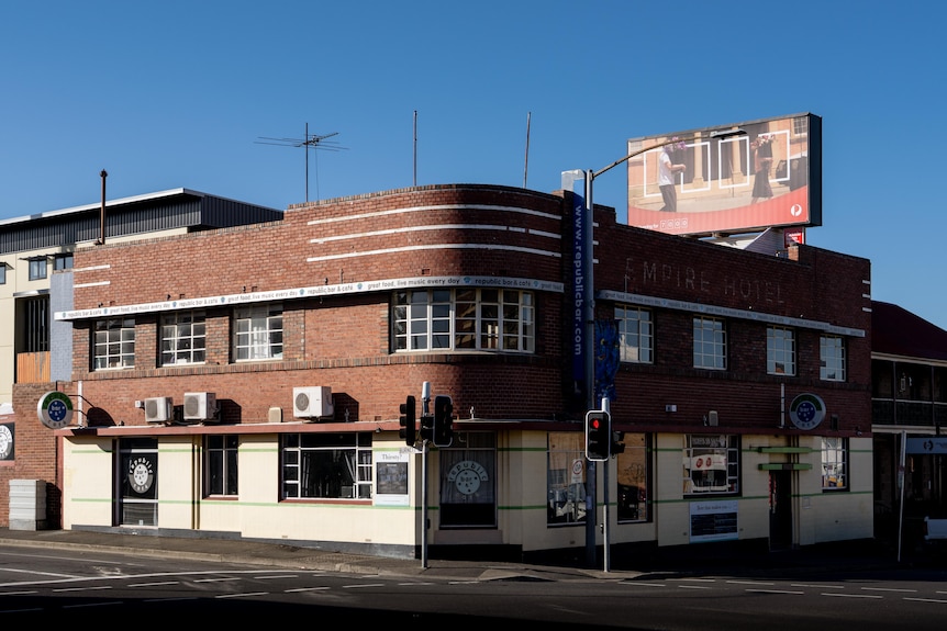 Wide shot of venue on the corner of a road with traffic lights flashing red in front, the venue is red brick and yellow.