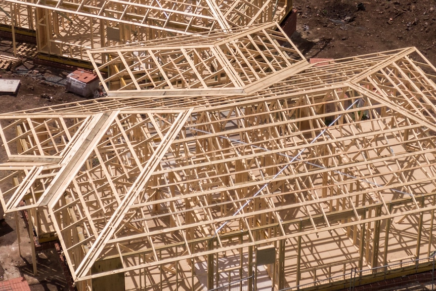 An aerial shot of two wooden house frames. Piles of red bricks are scattered around.