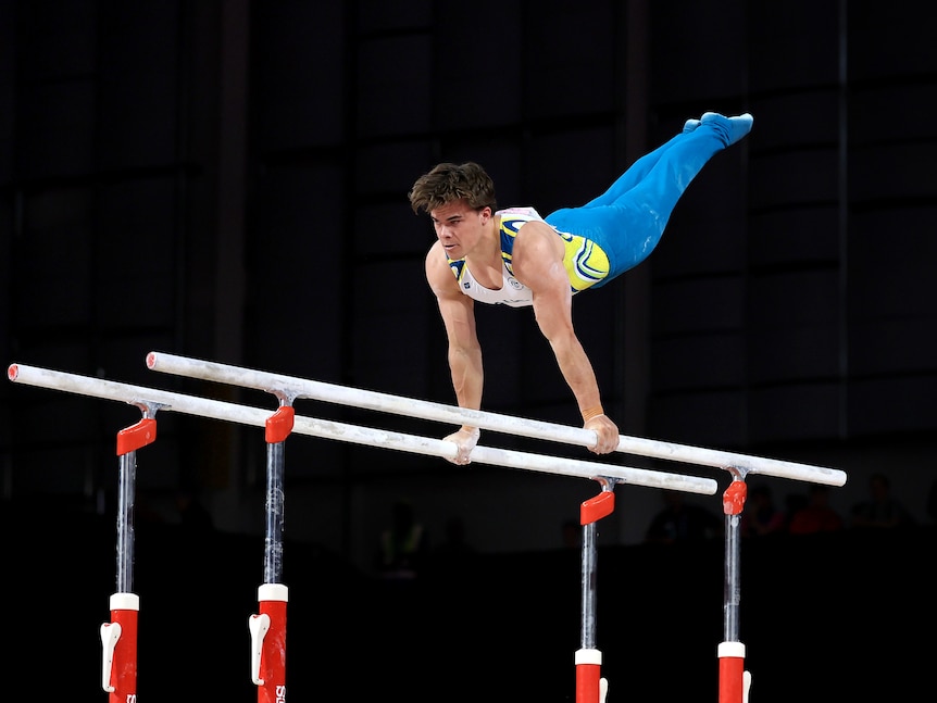 Jesse Moore holds on to two bars as he holds himself in the air mid-routine.