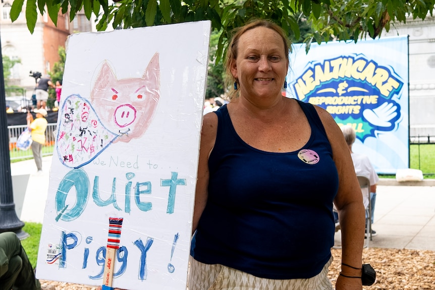 Stacy Nichols holds a protest sign that says 'We need to quiet piggy'.