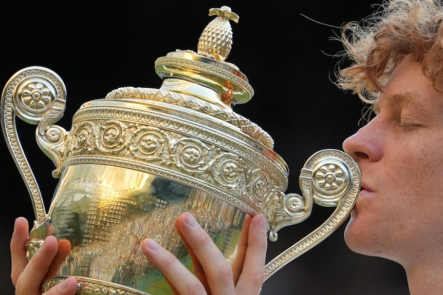 Jannik Sinner kissing a golden trophy.