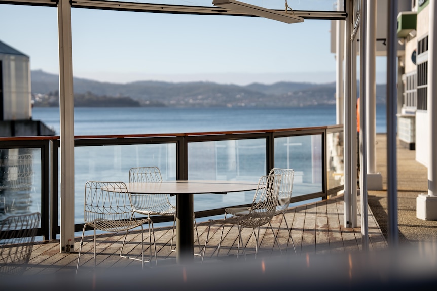 A table and chairs on an undercover balcony looking out to the Hobart waterfront on a sunny day.
