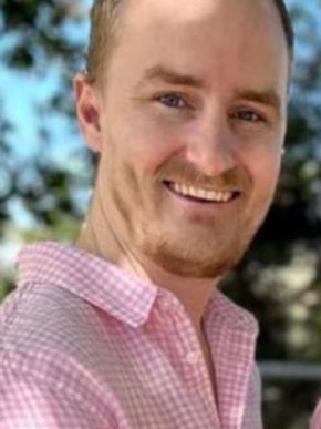 Mid 30s man in pink checkered shirt, stubble facial hair, smiling at camera,