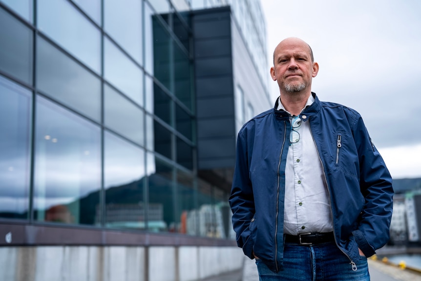 A man dressed in blue stand outside a building with grey skies.