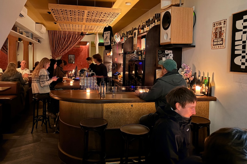 Poeple sit at tables and bar in dimly lit bar