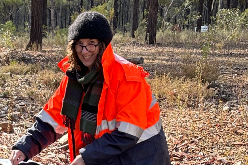 Louise kneels on the ground in the bush, wearing high vis.