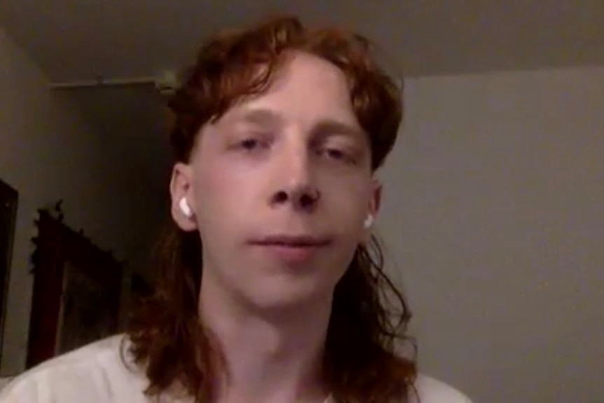 Young man with long, wavy, reddish hair smiles.