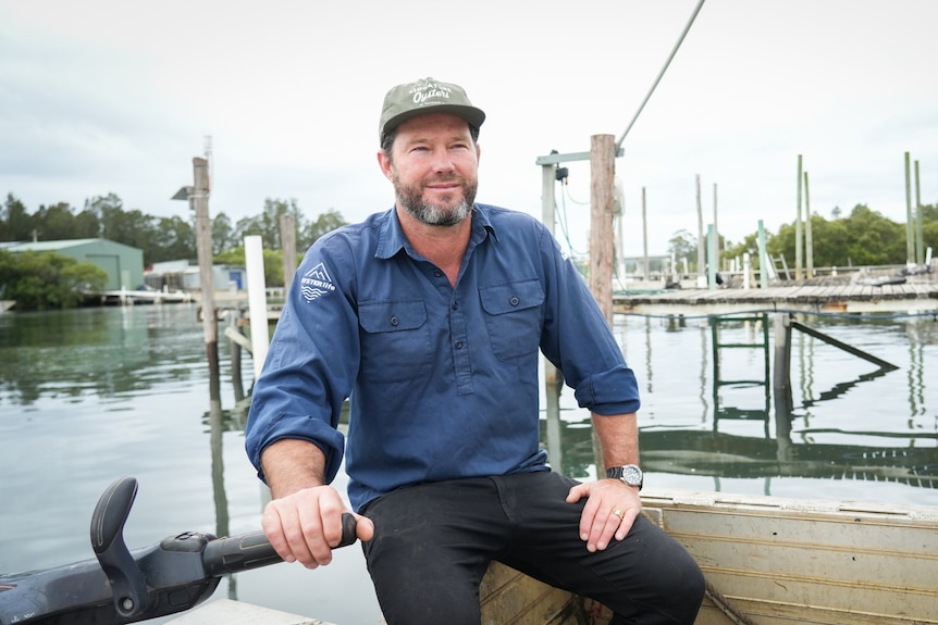 A man on a boat with a marina behind him.