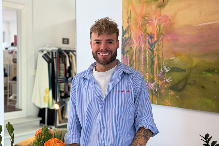 A man in a blue shirt standing next to a painting.
