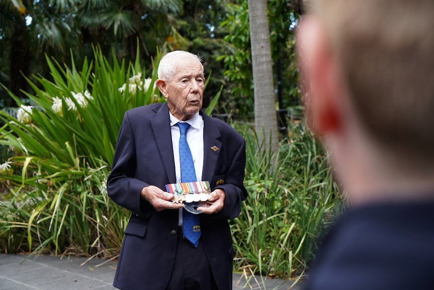 A man in a navy suit holds medallions. 