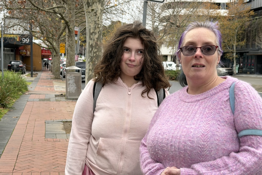 A woman wearing a pink jumper stands with a younger woman wearing a cardigan.