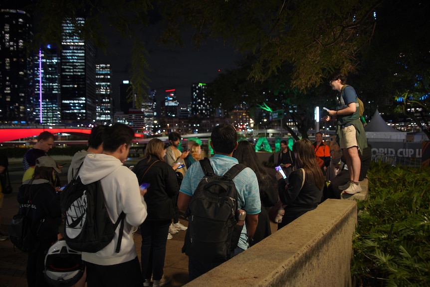 A man stands on a small wall in front of a group of people