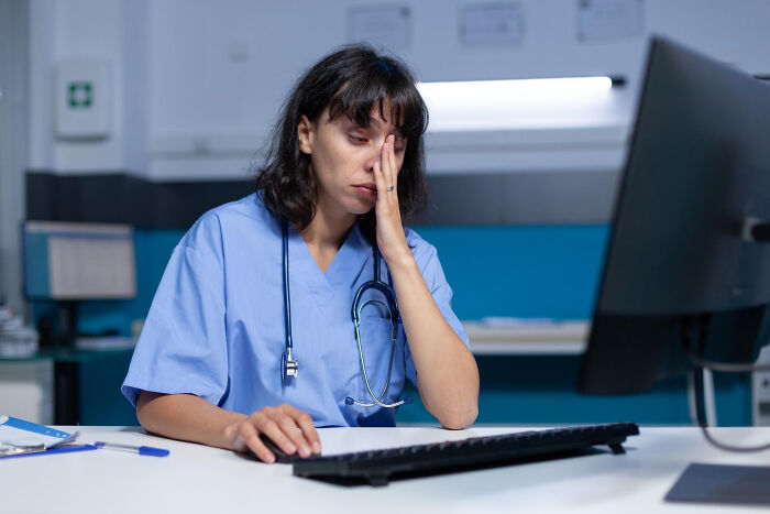 Tired nurse working on a computer, reflecting on uncomfortable truths within the medical industry.