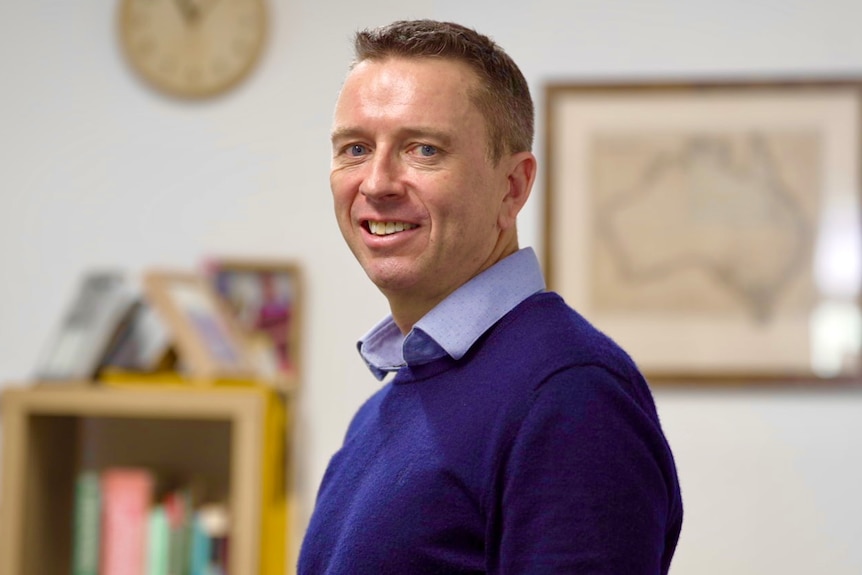 Man wearing purple jumper poses in a home office