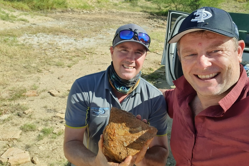 Two smiling men holding a fossil in the desert.