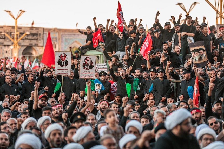 Large crowd wearing black clothes and holding red flags at a funeral ceremony.