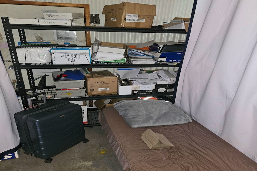 A mattress on the floor of a small room with metal shelves behind it.
