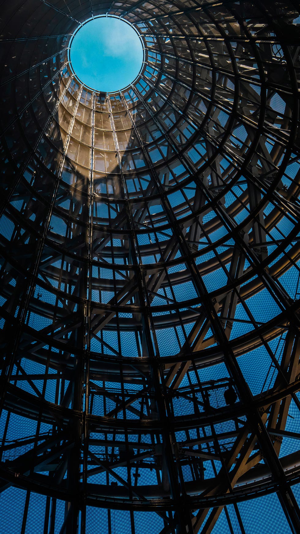 View looking up at a circular skylight within a modern architectural structure against a blue sky.
