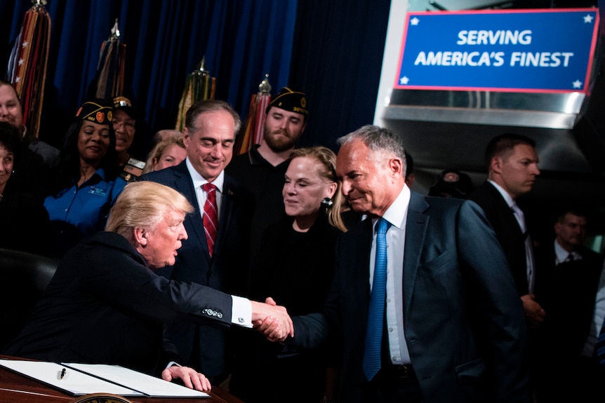 Donald Trump shaking hands with another man.