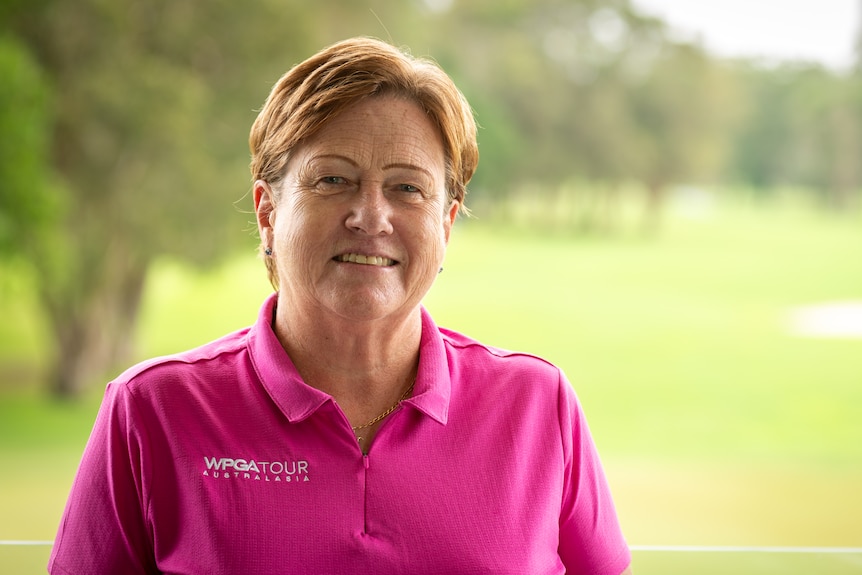 A woman in a polo shirt in front of a golf course.