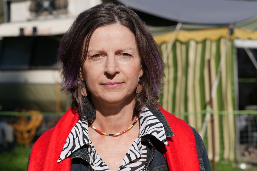 Woman with short hair and purple highlights, with a red scarf draped on her shoulders.