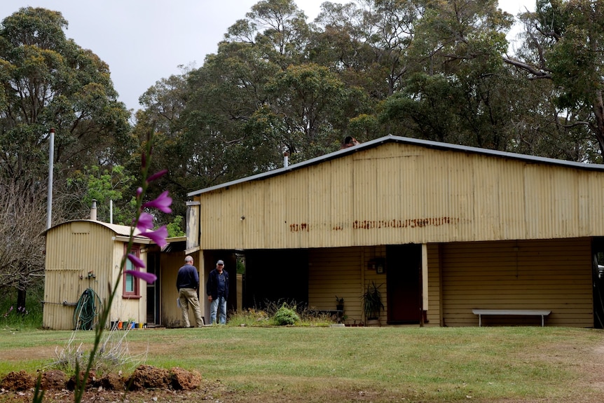 A wide angle picture of an old tin shed , barracks with two older men in foreground