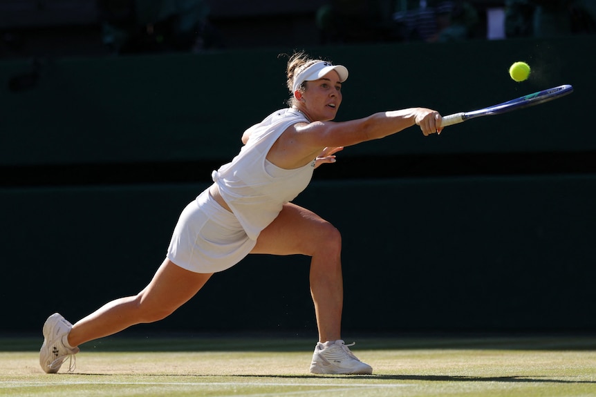 A young woman stretches out to make a backhand shot on a tennis court.