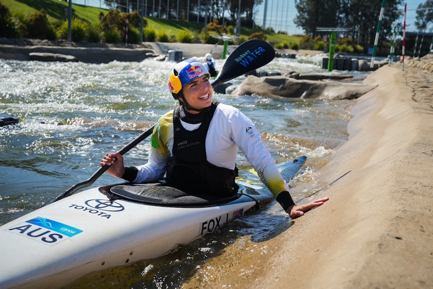A young woman in a canoe on the water smiles to the side.