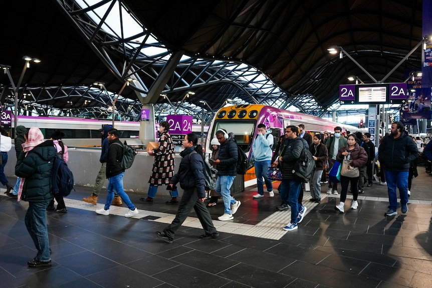 People walk on a station platform after getting of a purple regional train.