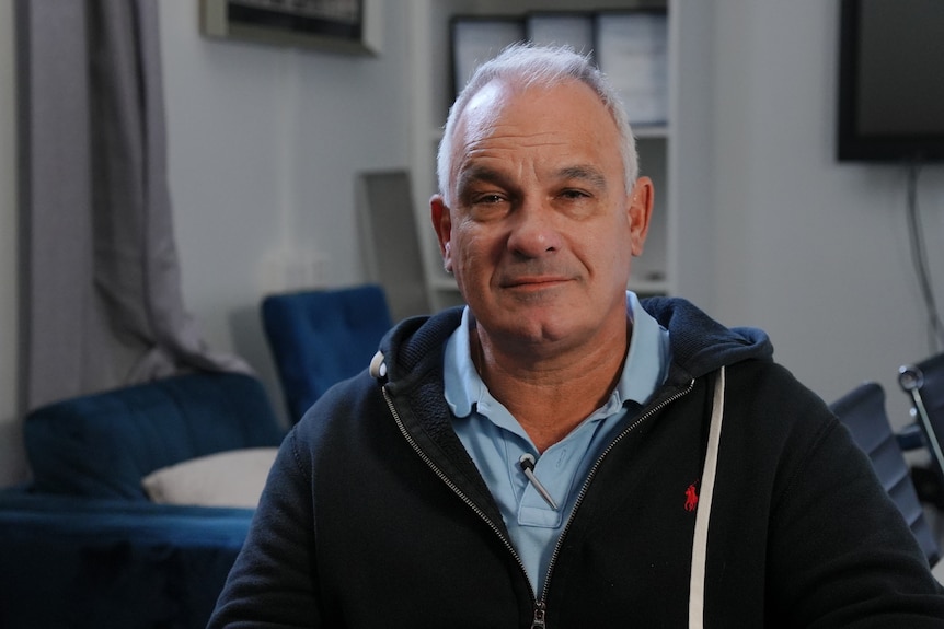 A man with grey hair in a dark hoodie looking at the camera inside a conference room.