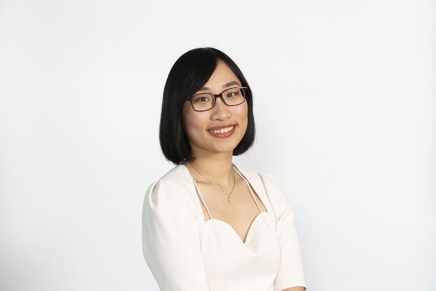 A woman wears glasses and dresses in a white top.