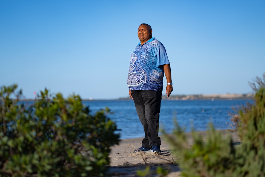 Ngarrindjeri elder Mark Koolmatrie stands on the sand dunes at the Coorong's blue waterside on a sunny day