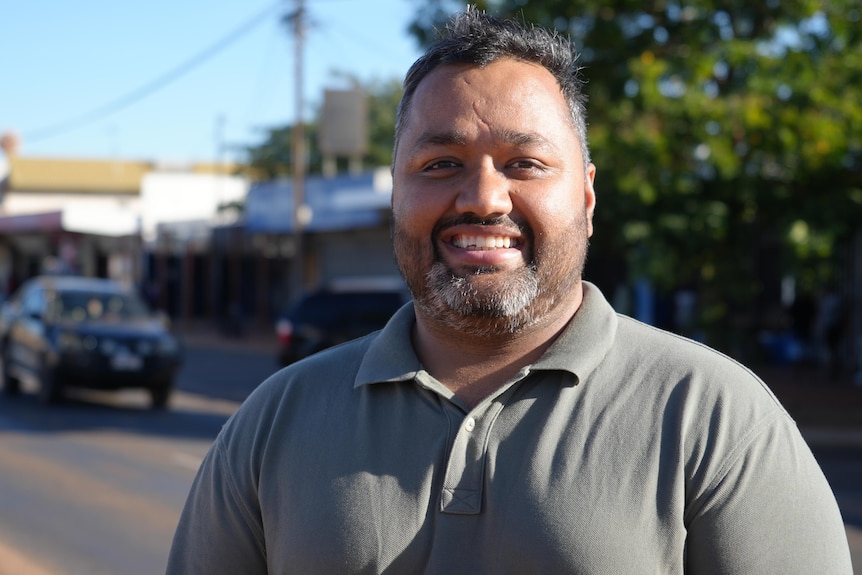 Sid Vashist with black hair and beard, standing on central street, smiling in sun.